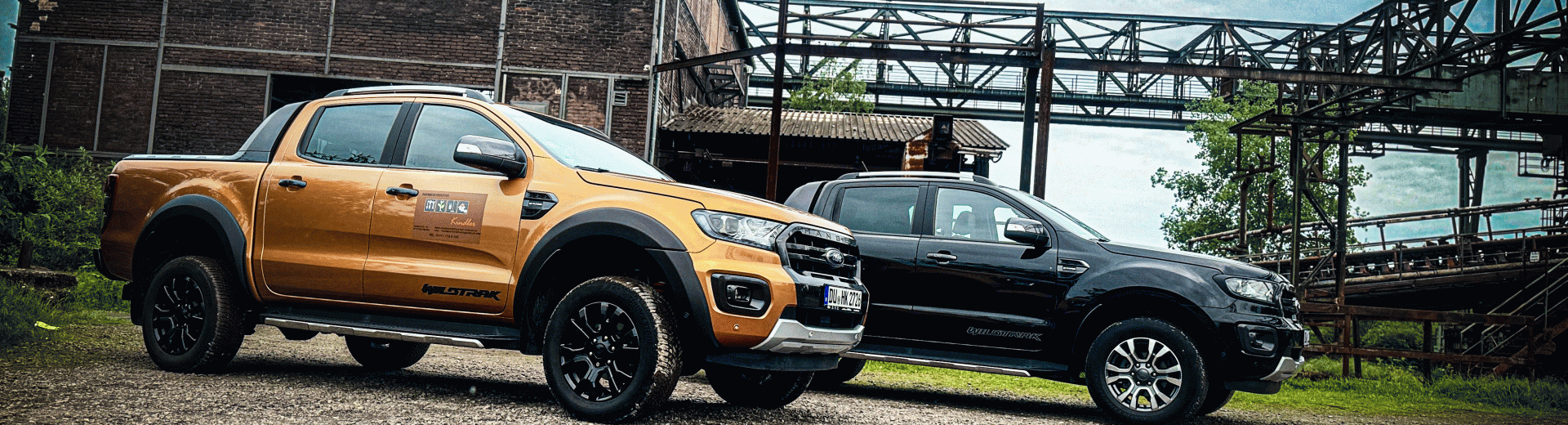 Zwei Ford Ranger Pick-up-Trucks stehen nebeneinander in einer industriellen Umgebung.